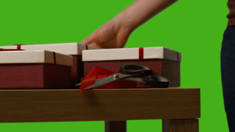 Close-Up-Of-Man-Gift-Wrapping-Presents-In-Boxes-Decorated-With-Ribbon-On-Table-Shot-Against-Green-Screen-2